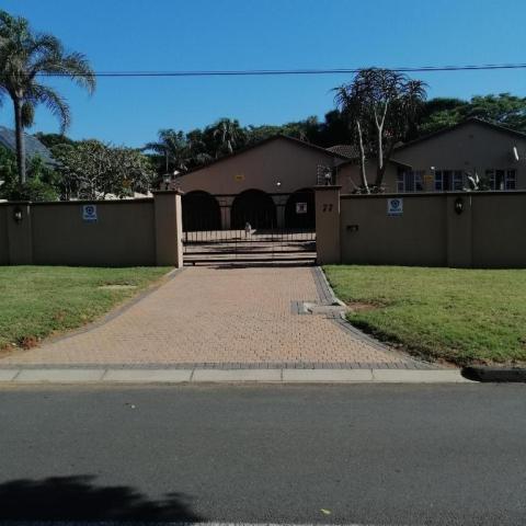 Gated residential house with palm trees and a brick driveway.