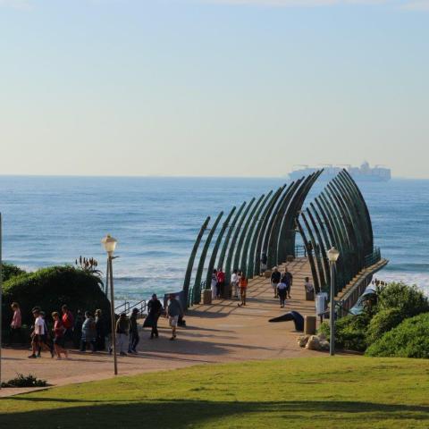 People walking on a pier with arch structures by the ocean.