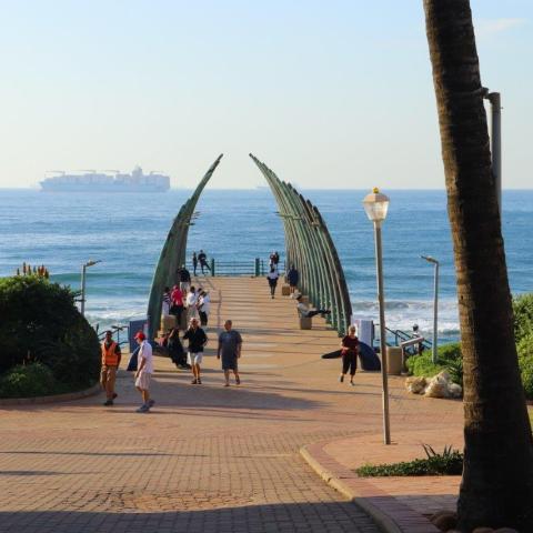 People walking on a pier with curved supports and ship in the ocean.