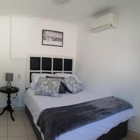 Small, modern bedroom with a double bed, gray bedding, side table, and wall-mounted air conditioner.