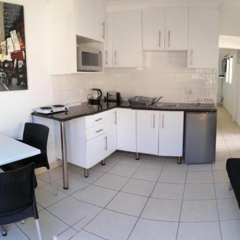 Compact kitchen with white cabinets, table, chairs, couch, and wall art.
