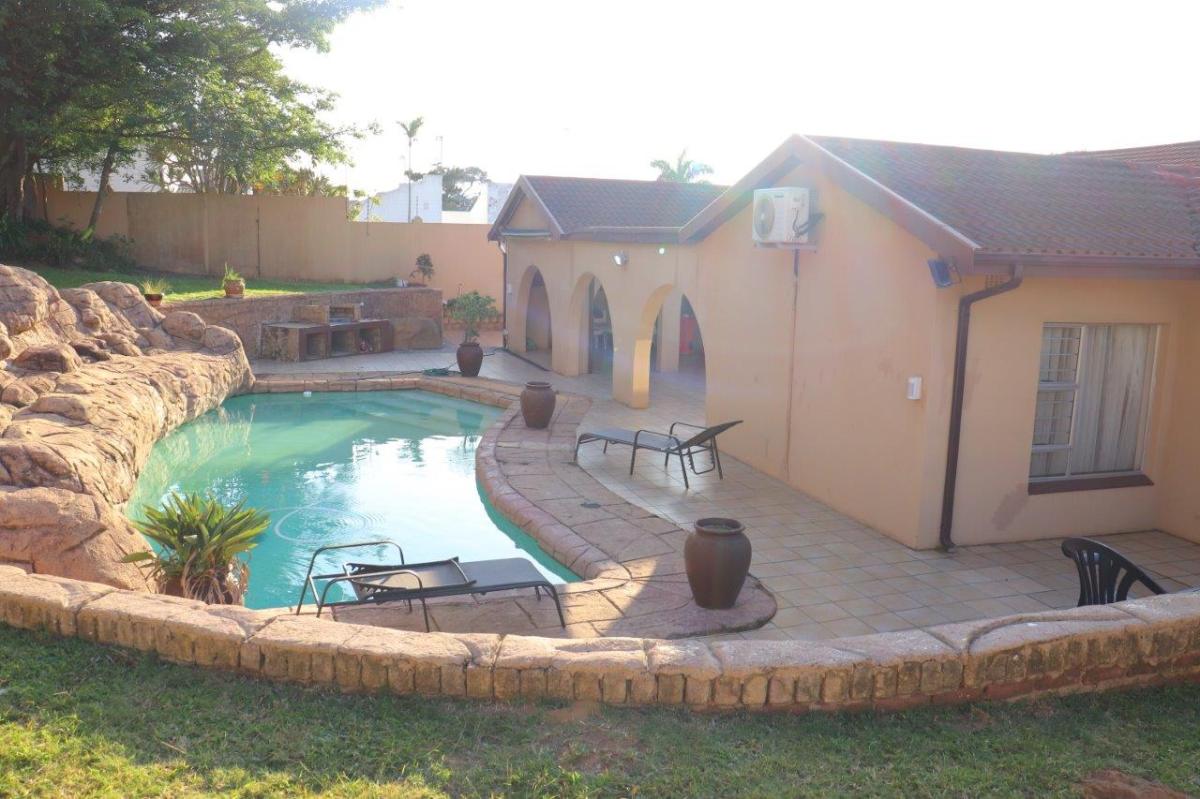 House with pool, patio, and tropical plants in a sunny yard.