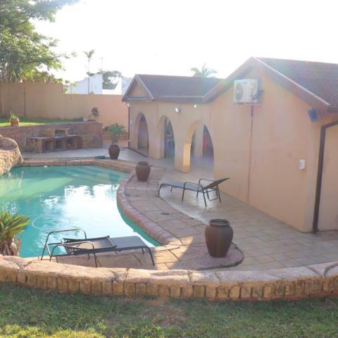 House with arched patio, curved pool, rock waterfall, and garden.