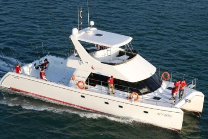 White catamaran boat with people in red shirts on blue water.
