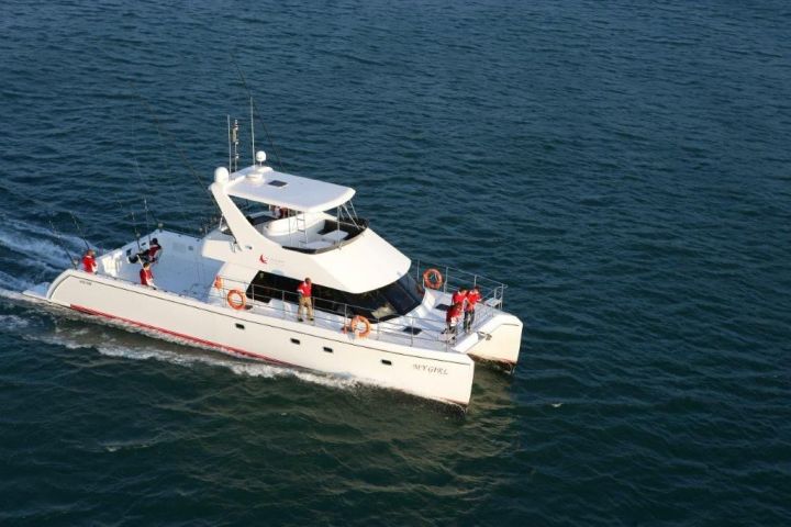 White catamaran with people in red outfits sailing on open water.