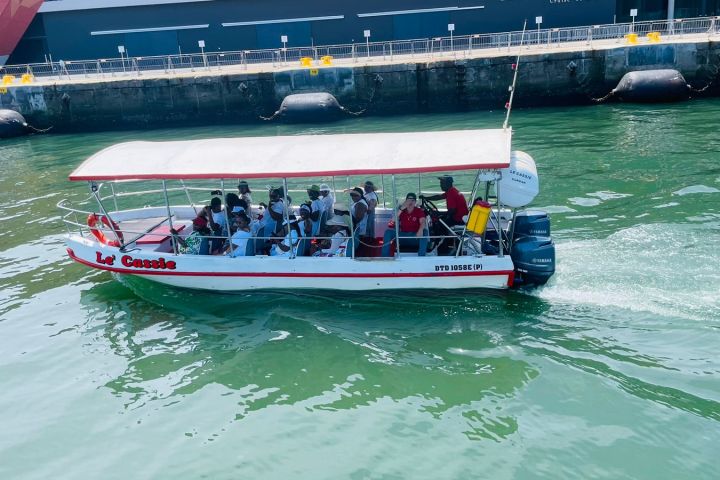 Small boat with canopy carrying passengers on green water near a dock.