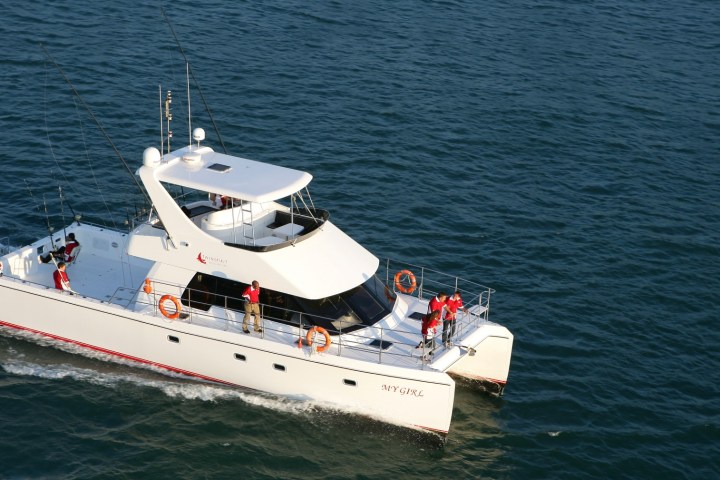 A white yacht with people on board sailing on calm blue waters.