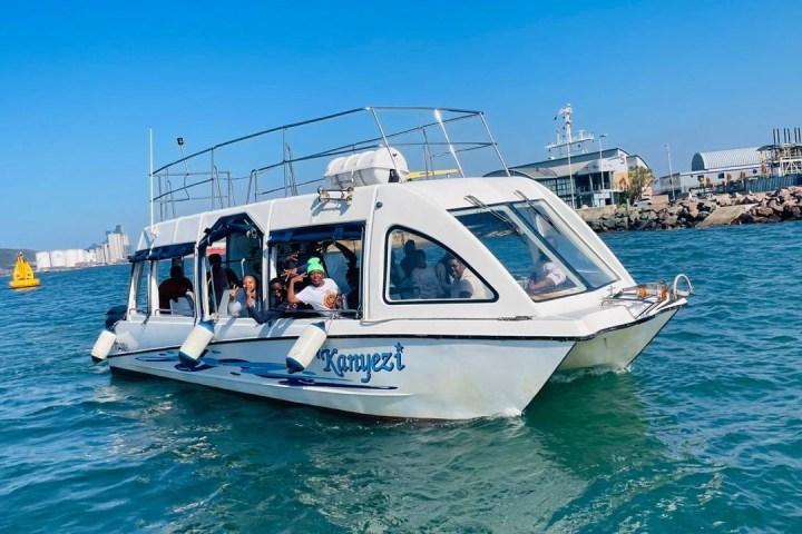 White tour boat on water with passengers, near a marina on a sunny day.