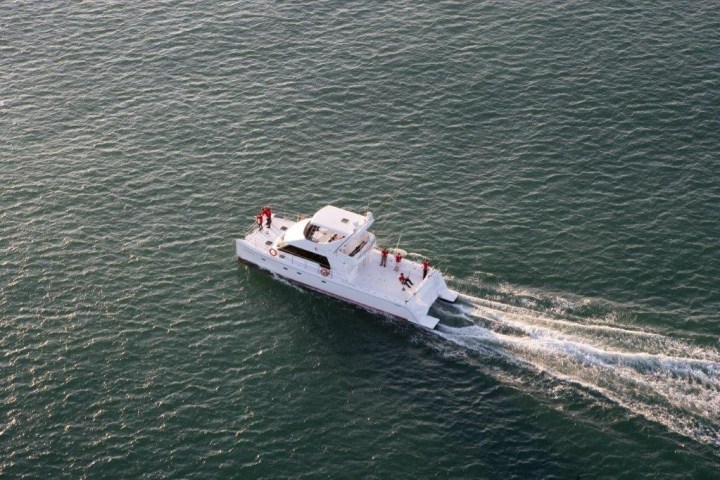 Aerial view of a white catamaran boat with people on a calm sea.
