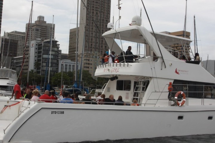 A white yacht with people on board floats near city buildings and other boats.
